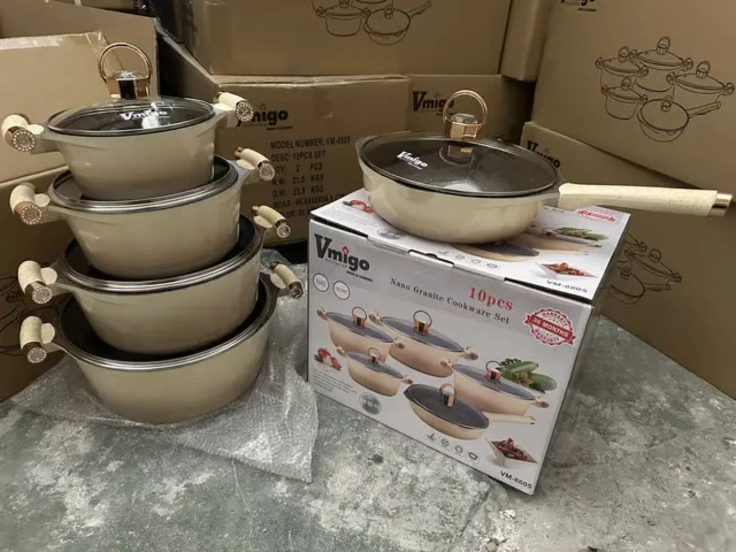 Set of cookware with lids on a box labeled 'Vimigo' on a gray surface.