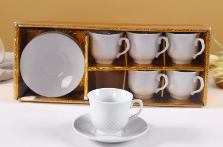 Set of white ceramic cups and saucers in a decorative box on a light surface.