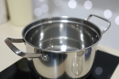 Stainless steel pot on a cluttered surface with various items in the background