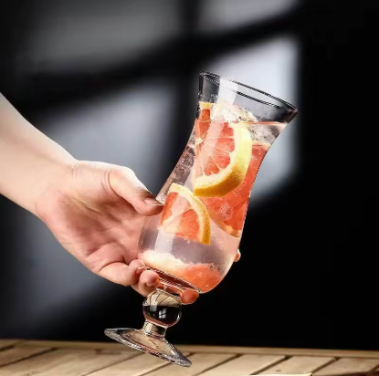 Hand holding a glass of pink cocktail with grapefruit slices against a dark background