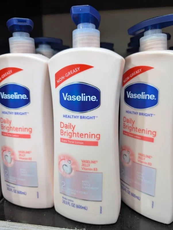 Three bottles of Vaseline Daily Brightening lotion on a black surface.