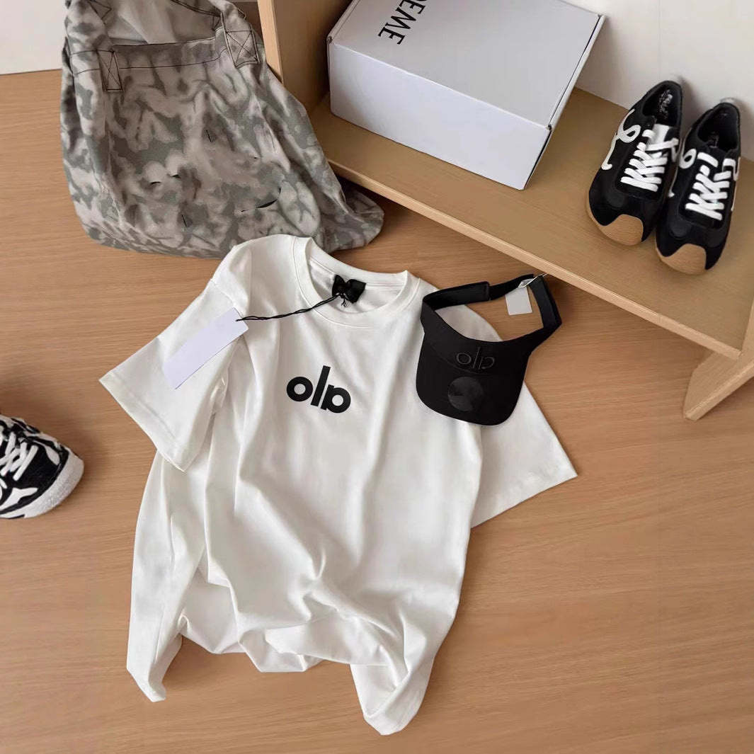 White t-shirt with 'olb' logo, black visor, camouflage bag, and black sneakers on a wooden surface.