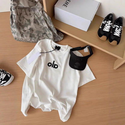 White t-shirt with 'olb' logo, black visor, camouflage bag, and black sneakers on a wooden surface.